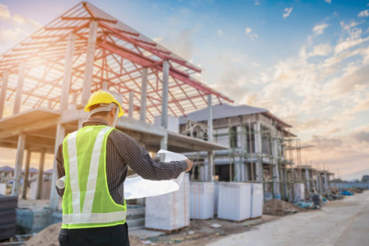 architect with protective helmet and blueprints at construction site