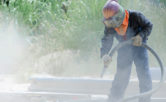 worker removing paint by air pressure sand blasting