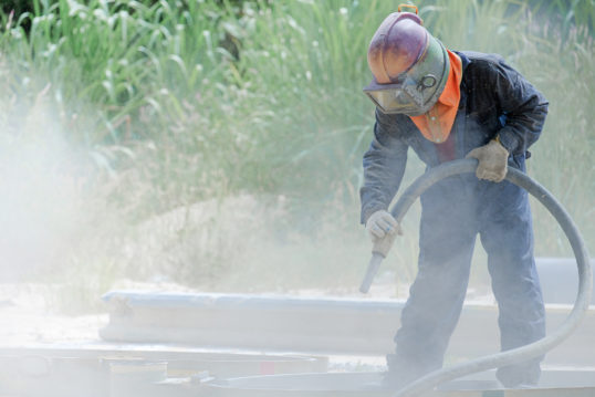 worker removing paint by air pressure sand blasting