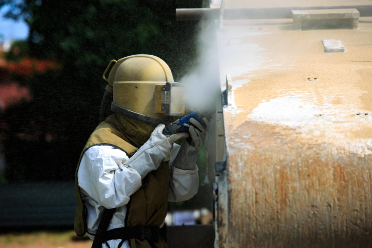 worker removing paint by air pressure sand blasting