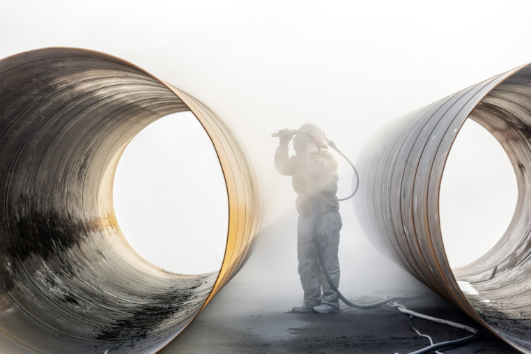 person sandblasting the pipe materials