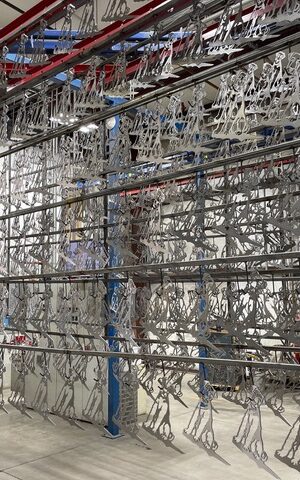 dozens of metal dog cutouts hanging from a powder coating rack on a factory floor