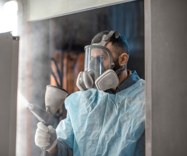 AR-powderimage6optimized a man in a ventilated face mask and blue protective clothing spraying powder coating onto a surface
